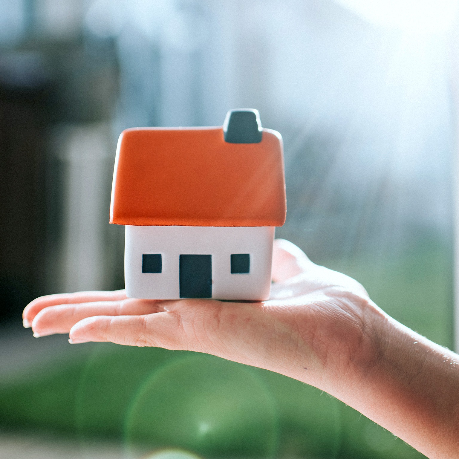 Model of a house with a red roof, held on a palm