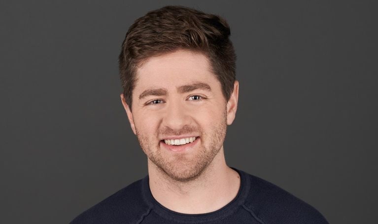 Eric Glyman with short brown hair and a trimmed beard smiling during an interview. He is wearing a dark jacket over a light-colored shirt, with a softly blurred indoor background behind him.