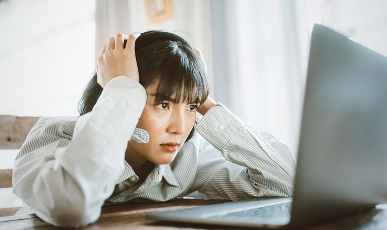This image shows a person appearing stressed or frustrated while working on a laptop computer, representing professional challenges.