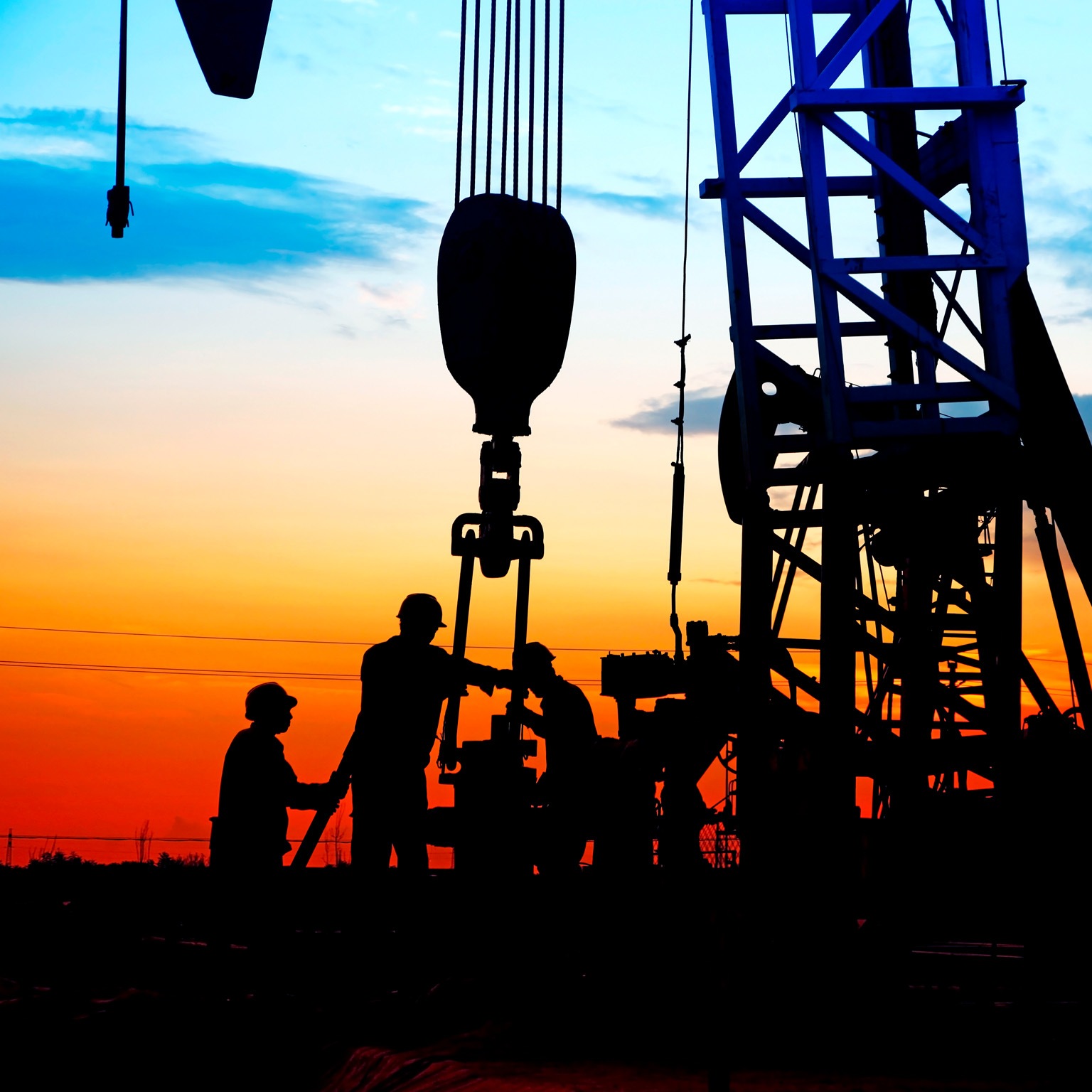  Silhouetted workers operating an oil drilling rig, against a vivid sunset sky with gradients of orange, red, and blue.