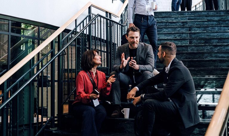 Two men and a woman sitting on the staircase landing engaged in a discussion