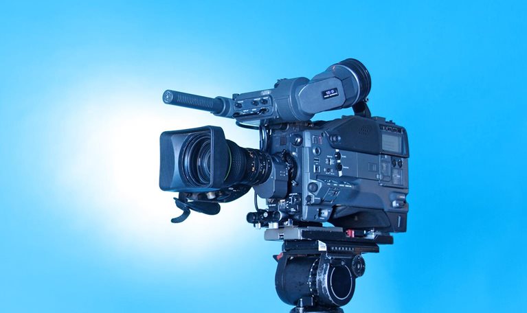 A professional video camera on a tripod with a rich gradient blue background.