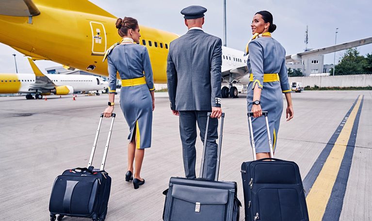 A low-angle view of a flight crew walking towards an airplane pulling their luggage with them.