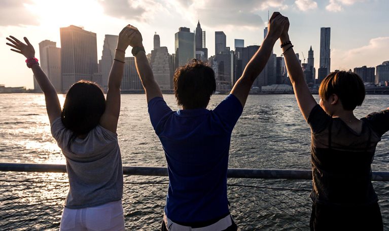 Three friends holding hands in celebration across the water from a city skyline