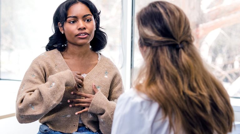 The young adult woman gestures as she explains her symptoms to the unrecognizable female doctor.