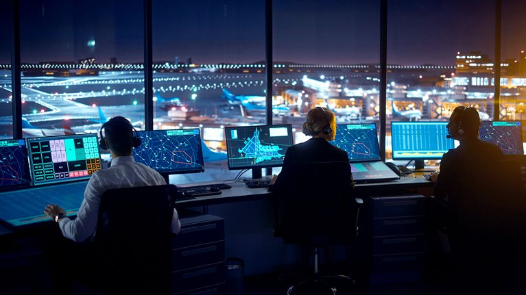 Diverse Air Traffic Control Team Working in Modern Airport Tower at Night. Office Room Full of Desktop Computer Displays with Navigation Screens, Airplane Departure and Arrival Data for Controllers. - stock photo