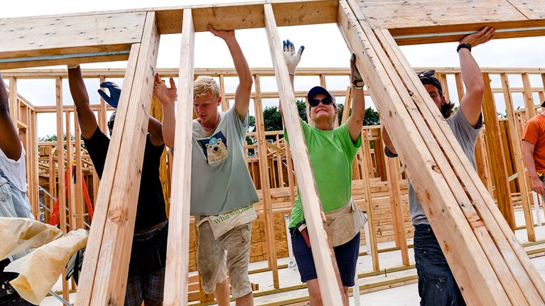 Volunteers lifting framed wall at construction site - stock photo