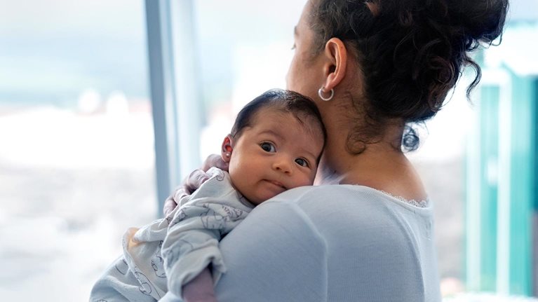 The mother is on her back looking out the window while holding the baby in her arms. The baby is looking at the camera. Concept of protection. - stock photo