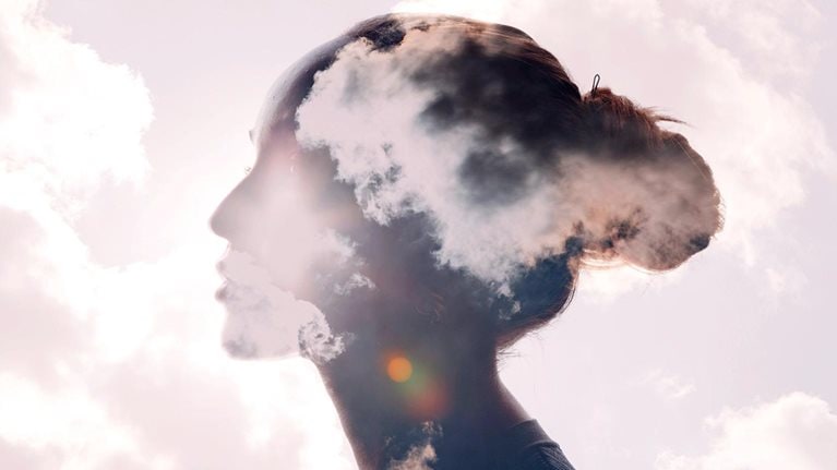 Illustration featuring a silhouette of a woman's head with a sunrise and cloud multiple exposure background.