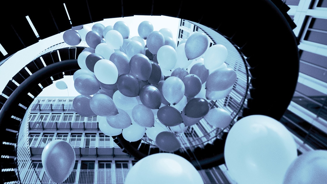 Image of many balloons tied together, floating up through an outdoor spiral staircase