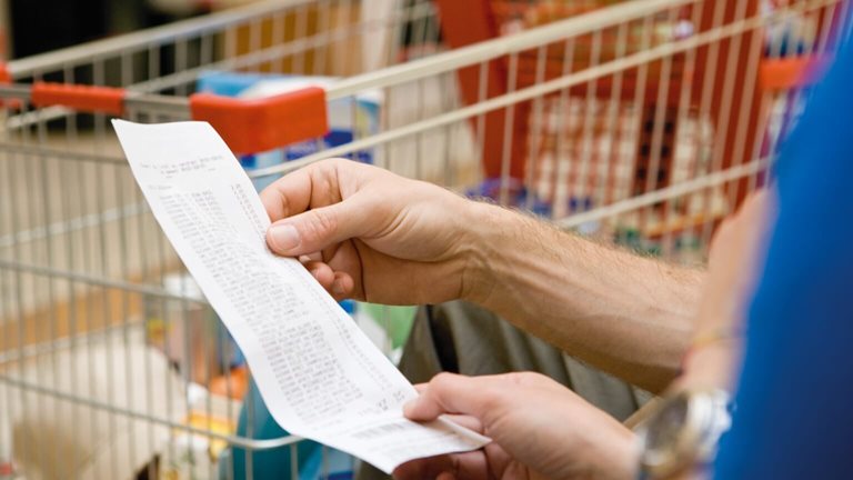 photo of hand holding grocery receipt in front of shopping cart