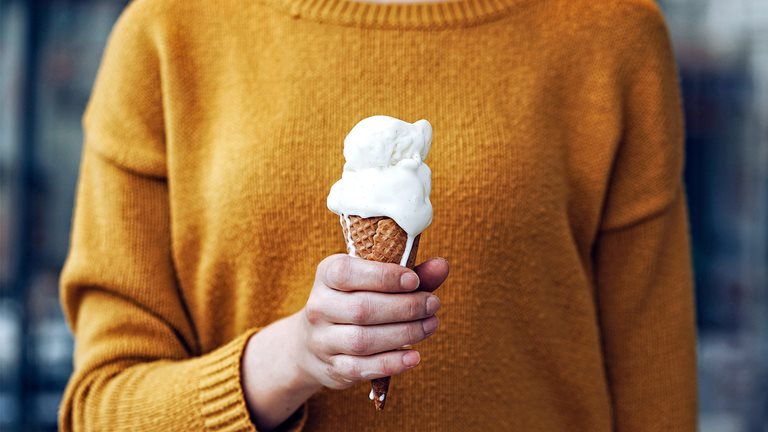 Image of a woman in yellow sweater holding a melting ice cream cone in her hand