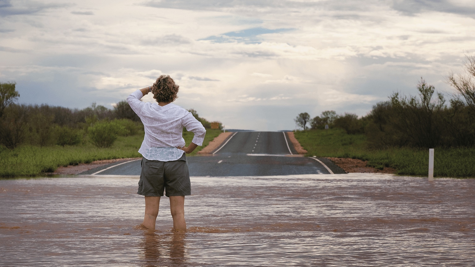 Image of a woman standing in flood waters, looking at a road