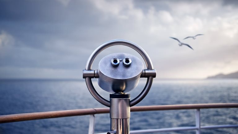 Telescope on a ship with two birds flying over the water in the background