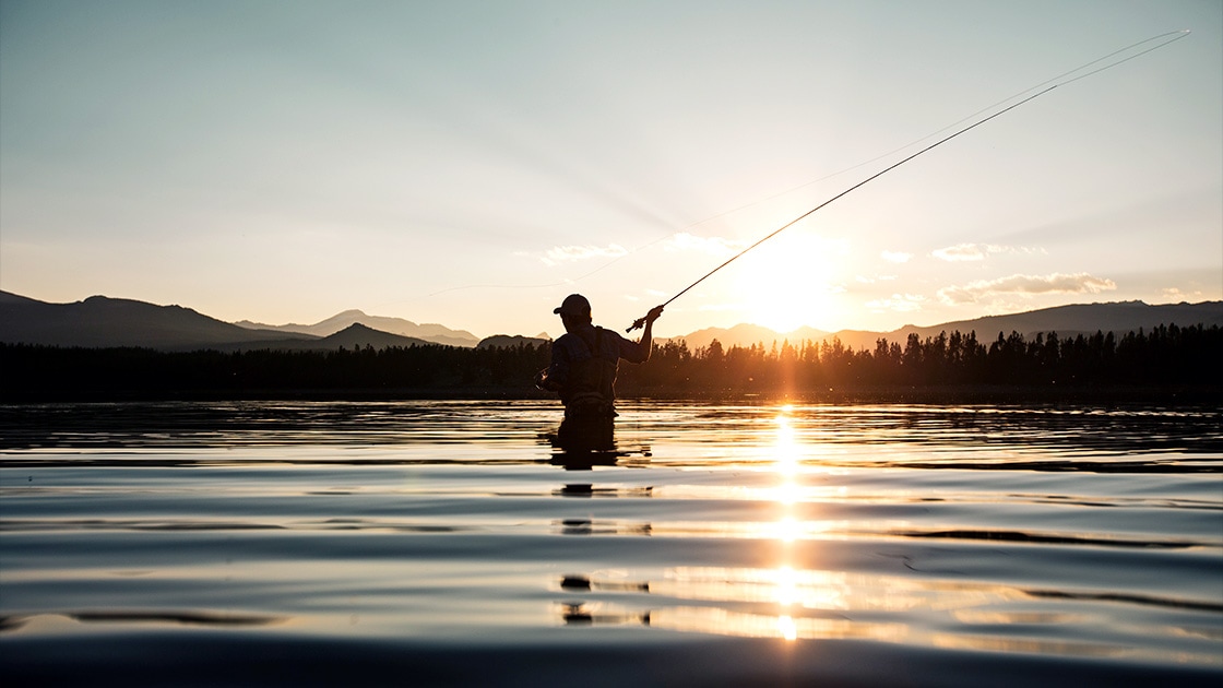 Person swinging a fishing pole in water at dusk