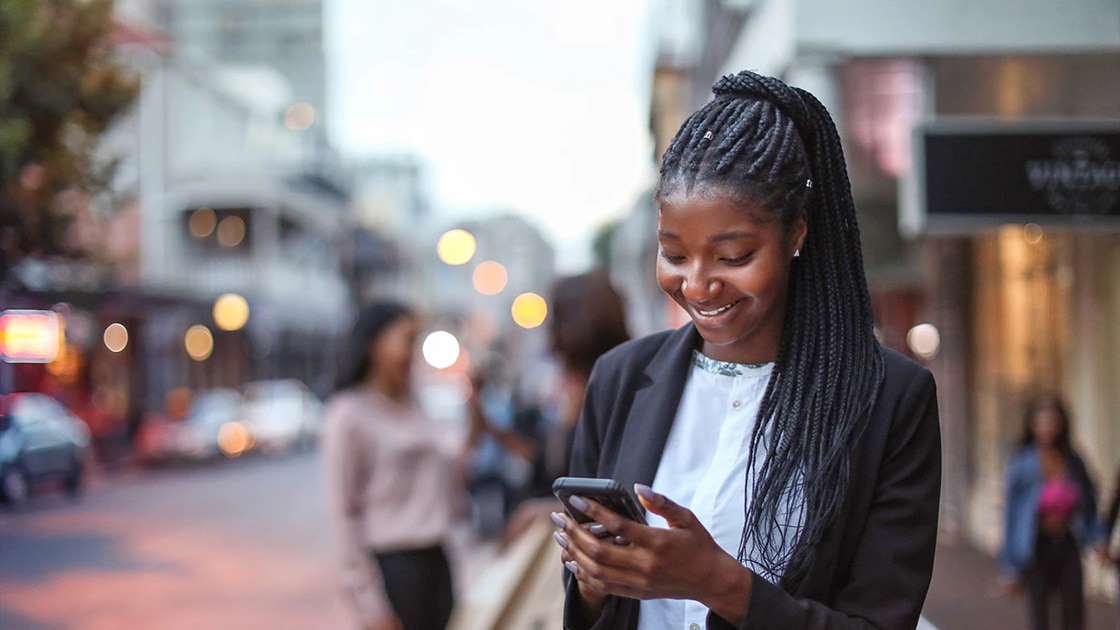 Image of a Black woman looking at her phone in a shopping district