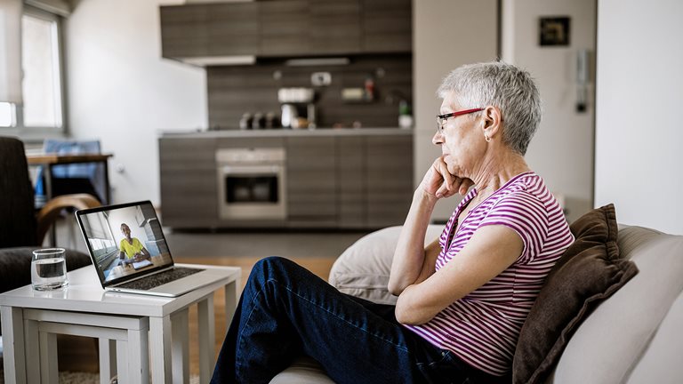 Older woman seated on couch watching something on her laptop