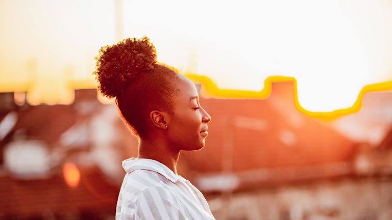 Image of young African-American woman relaxing on the rooftop with sunset light on her face