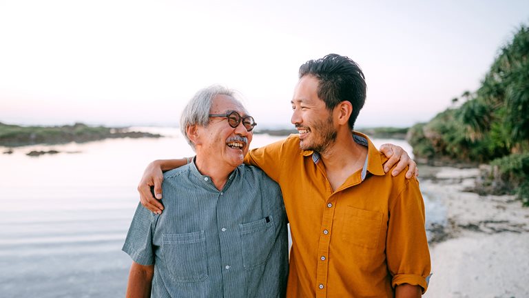 Image of senior father and adult son having a good time on beach at sunset