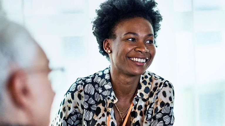 Cheerful woman in her 30s in business meeting with colleagues, smiling and listening, confidence, expertise, team player