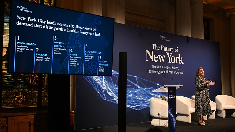 Lucy Pérez presents on stage beside a screen highlighting six dimensions of a healthy longevity hub at McKinsey & Company's The Future of New York event.