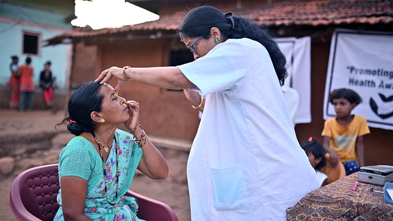 Doctor conducts an eye examination of a mid adult woman during a rural medical health care camp