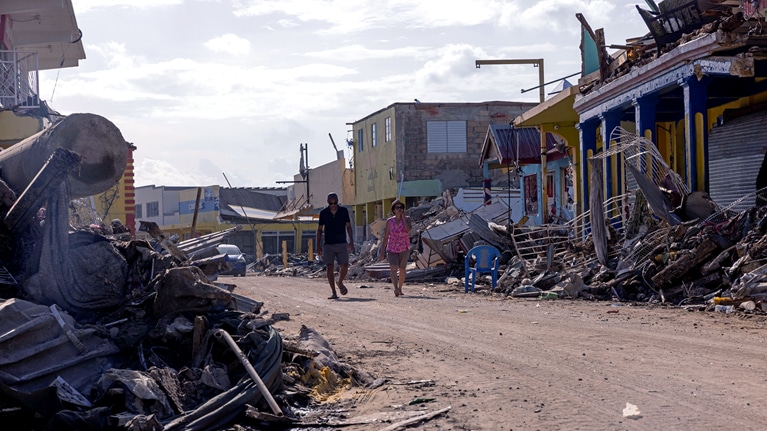 A man and a woman walking through an area devastated by a hurricane.
