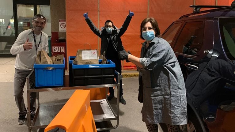 People in medical masks give thumbs up sign in front of carts of food for delivery