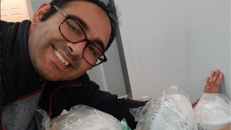 A smiling Asian man wearing glasses leans over packaged PPE