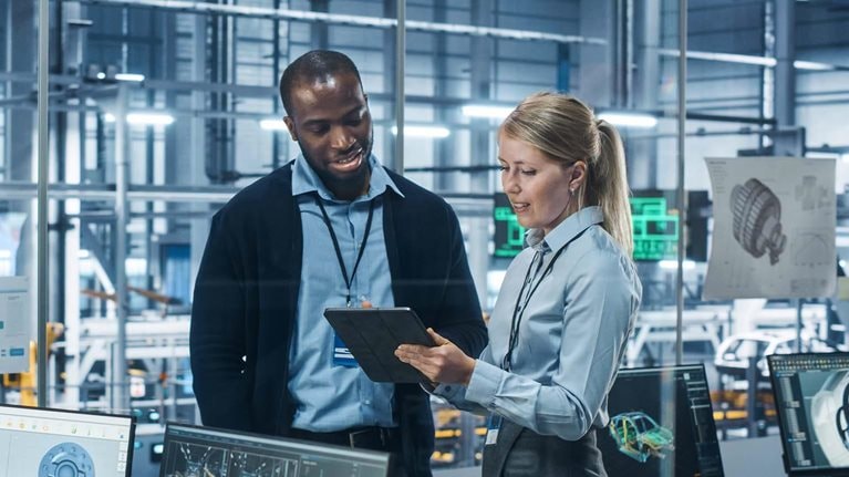 Car Factory Office: Female Engineer Talks with Male Scientist, Use Tablet Computer to Design Production Conveyor for Advanced Power Engines. Automated Robot Arm Assembly Line Manufacturing Vehicles