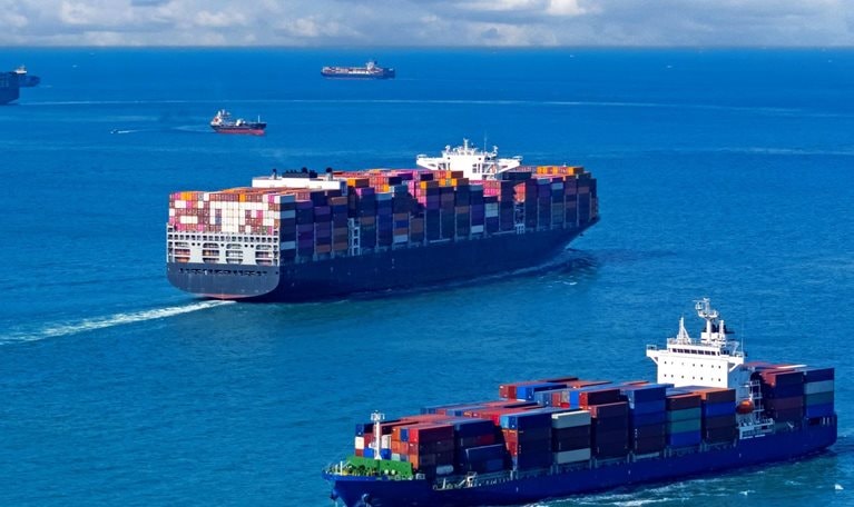 An image of several container ships navigating a vast expanse of blue ocean under a sky filled with fluffy white clouds.