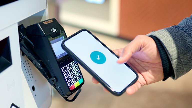 A person holds a smartphone near a payment terminal, with a checkmark displayed on the screen indicating a successful transaction.