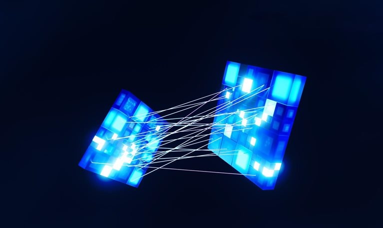 Two bright blue cubes, made up of smaller blue squares with digital patterns. Delicate white lines connect the cubes, giving the impression that they are being drawn together.