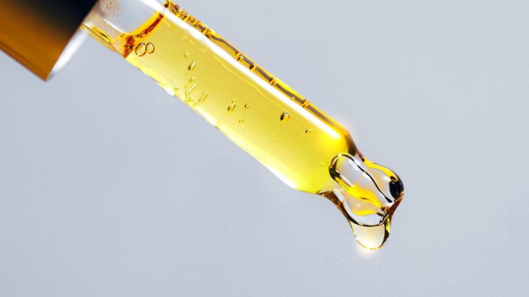 Closeup pipette dripping fragrant oil for cosmetic or spa procedure against grey background