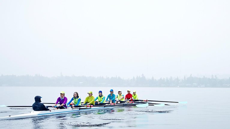 Group of mature female rowers rowing eight person boat during rainy morning practice