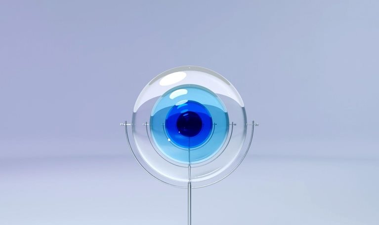 A sculpture made of four glass lenses, supported by delicate metal structures, creates an abstract display. The lenses, with their opaque blue hues and varying sizes, sway to eventually align and resemble an eye and iris.