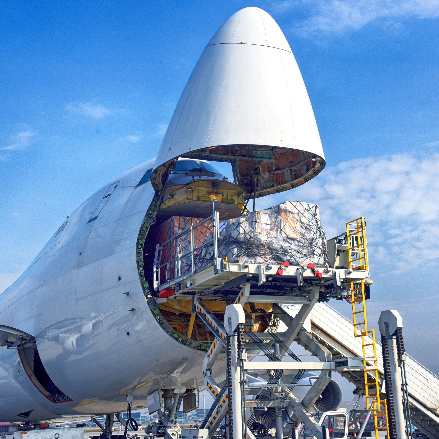 A cargo plane has its front end open as a sizable pallet is being loaded onto it.