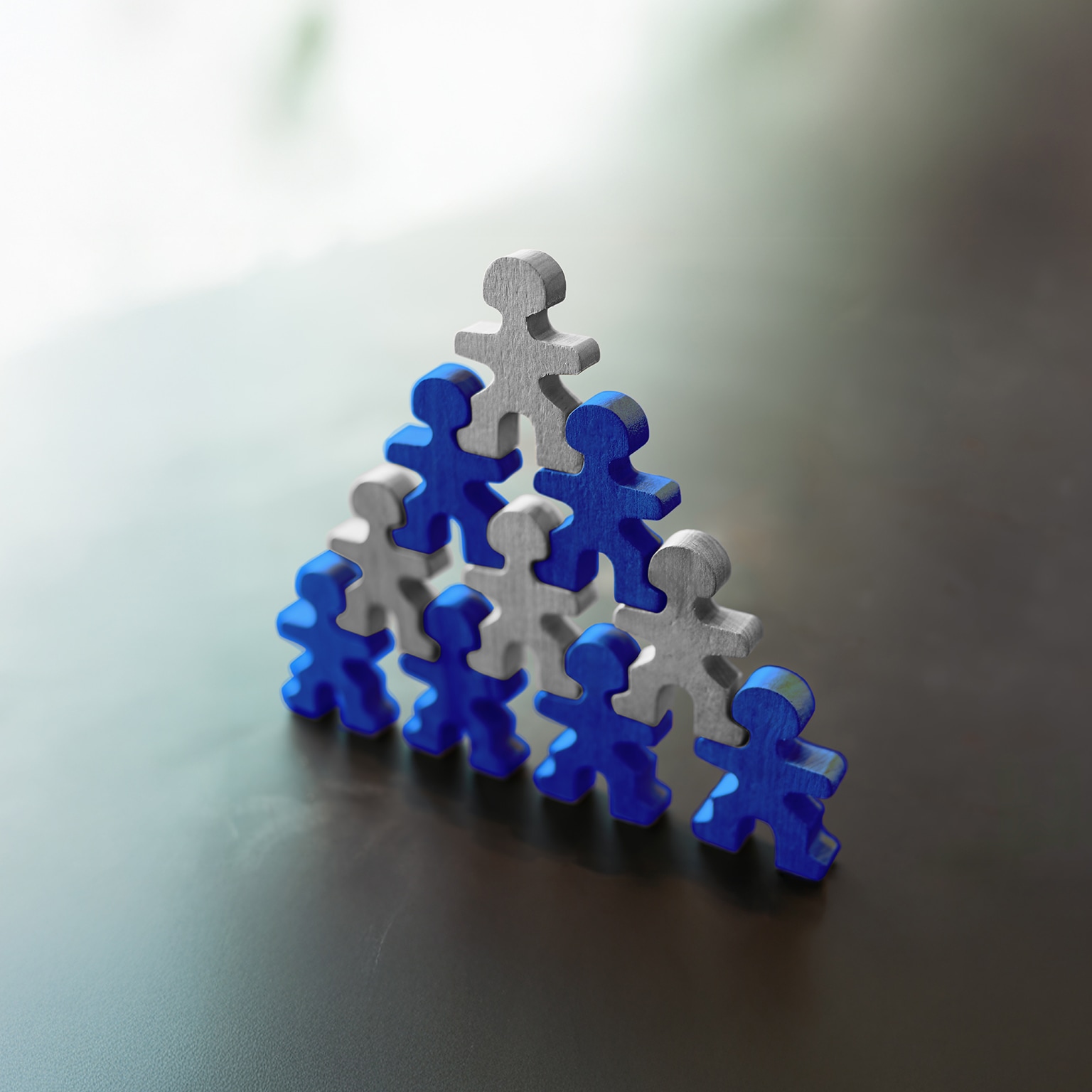 Wooden human figures forming a pyramid symbolizing teamwork, leadership, support, and organizational success. Concept of collaboration, unity, human resources, and business development.