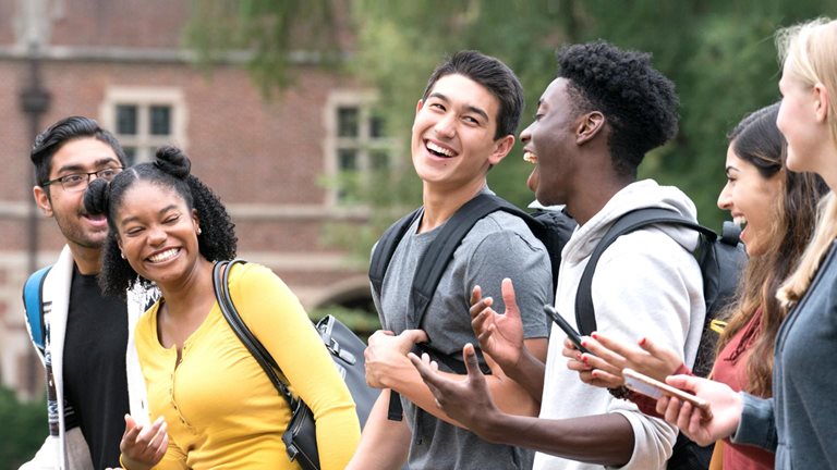 Photo of six students, wearing backpacks, laughing.