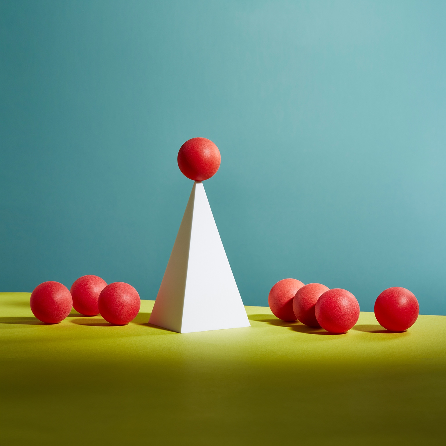 A red sphere balances on top of a white pyramid - stock photo