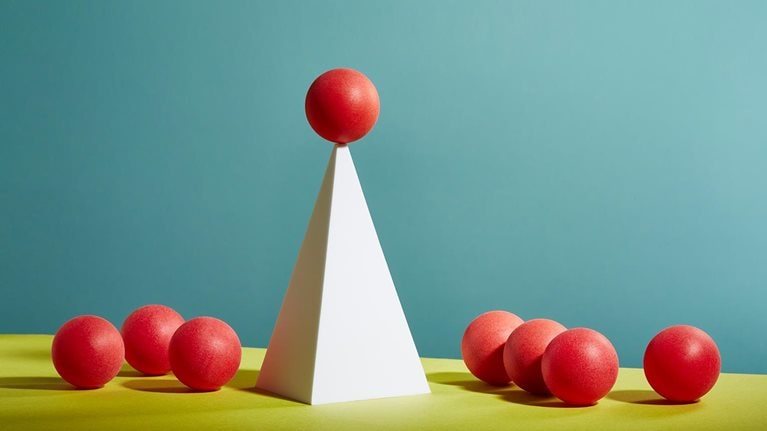 A red sphere balances on top of a white pyramid - stock photo