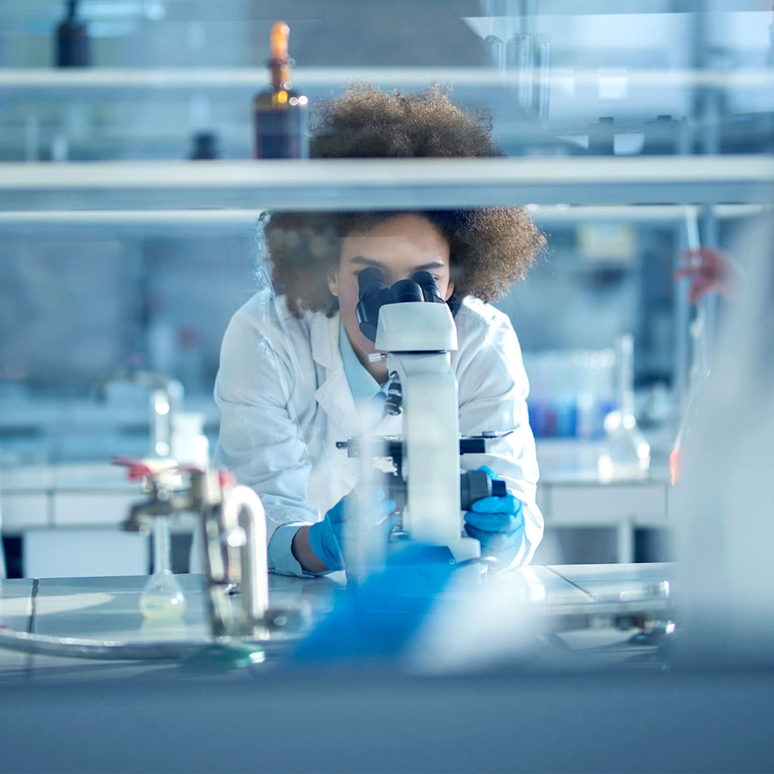 Young African American biochemist using microscope while working on scientific research in a laboratory. 