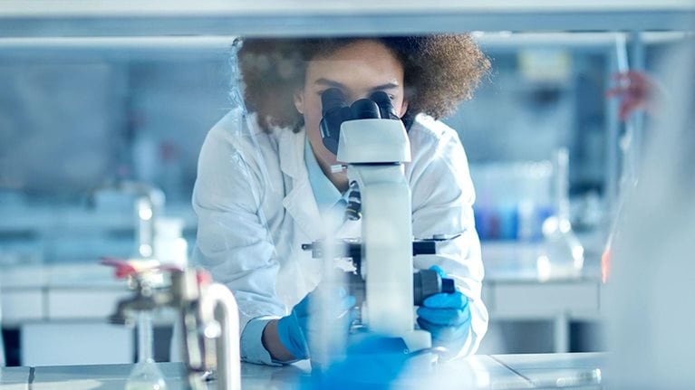 Young African American biochemist using microscope while working on scientific research in a laboratory. 
