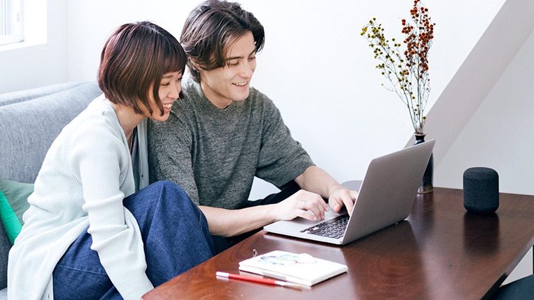 Couple sitting behind a coffee table in living room, using a laptop.