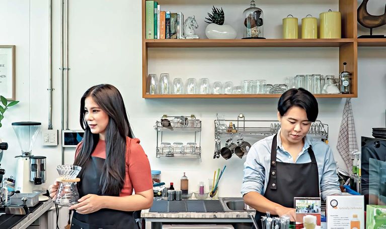 Two employees operating a modern café with professional coffee equipment and organized workspace