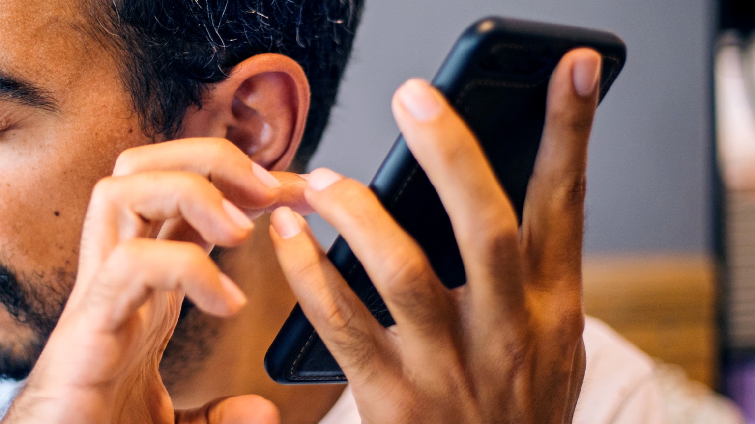 Close up photograph of both hands of a blind person who is holding a mobile phone up to his ear as he touches its screen.