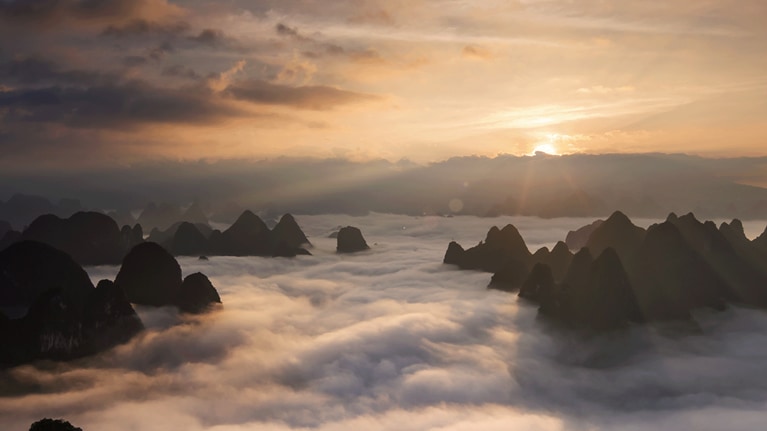 photo sun rising behind mountain, clouds in foreground