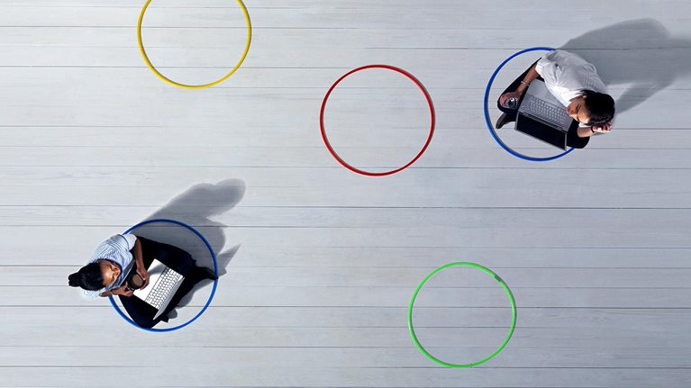 Business women with laptops sitting across the room from each other in 2 of 5 multi-colored circles