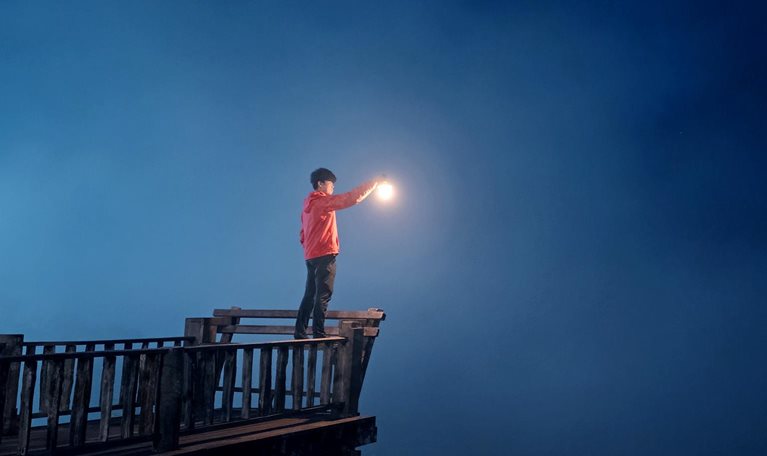 Image of a person holding up a lantern, peering into the misty darkness.