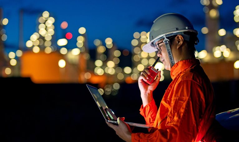 Industrial worker in overalls, helmet holding digital equipment such as laptop, walkie talkie, digital lamp
